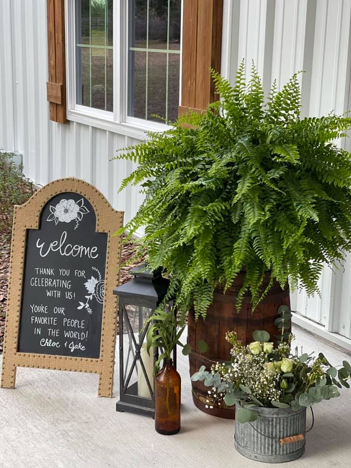 chalk sign welcoming guests to a wedding next to green plants and black lantern